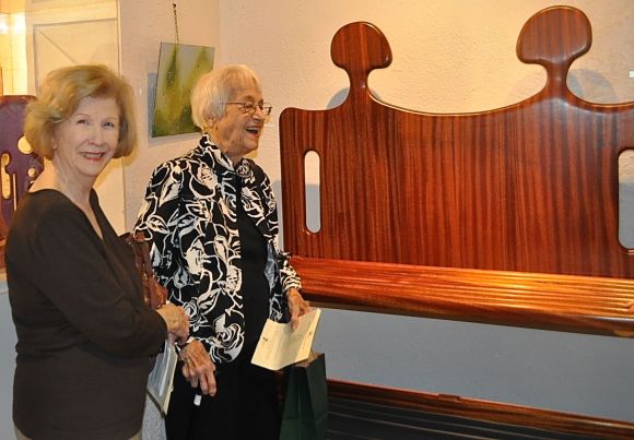Guests interacting over "Conversation Seat". Artwork in Mahogany wood.